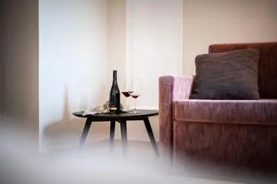 a bottle of wine and two glasses on a table next to a couch at Schloss Plars wine & suites in Lagundo