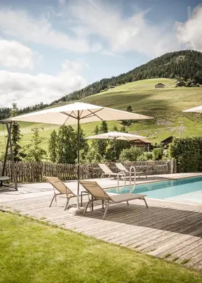 a swimming pool with chairs and umbrellas next to a pool at Falkensteiner Hotel & Spa Sonnenparadies in Terento