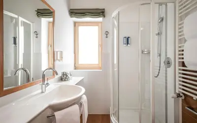 a white bathroom with a sink and a shower at Falkensteiner Hotel & Spa Sonnenparadies in Terento