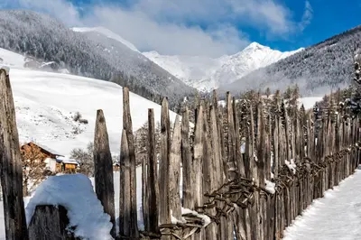 a wooden fence in the snow with mountains in the background at Falkensteiner Hotel & Spa Sonnenparadies in Terento