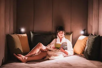 a woman sitting on a bed reading a book at Laurena Aparthotel in Naz-Sciaves