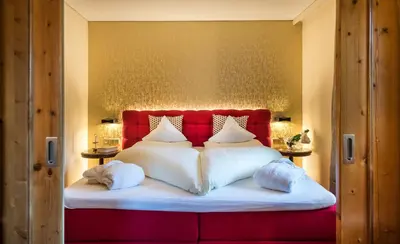 a bed with a red headboard and white pillows at Hotel Rosa Eco Alpine Spa in Alpe di Siusi