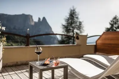 a patio with a table and a glass of wine at Hotel Rosa Eco Alpine Spa in Alpe di Siusi