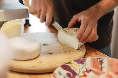 a man cutting a piece of cheese on a cutting board at Dolomitihouse BEDOL in Fiera di Primiero