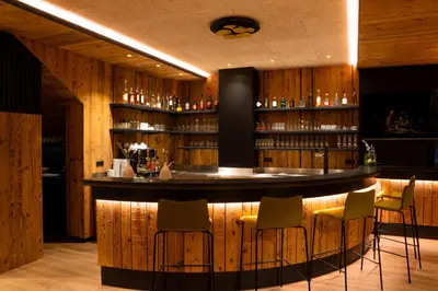 a bar in a restaurant with wooden walls and bar stools at Garni-Hotel mir.es in Tirolo