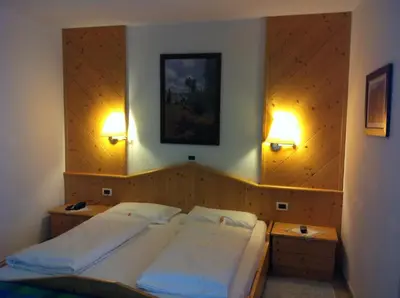 a bedroom with two beds and two lights on the wall at Piccolo Hotel Sciliar in Alpe di Siusi