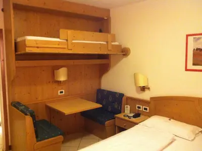 a room with a bed and a desk and bunk beds at Piccolo Hotel Sciliar in Alpe di Siusi