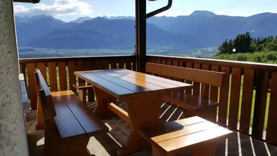 a wooden table and benches on a balcony with mountains at Dolomites White Rest - Mountain View in Tres
