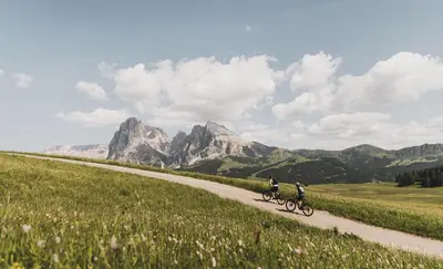 two people riding bikes down a dirt road with mountains at Apartment Weissenegger in Fiè