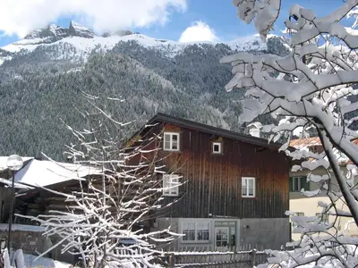 a wooden house with snow covered mountains in the background at Apartments Cableway Canazei in Canazei