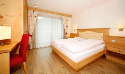 a bedroom with a bed and a desk and a window at Residence Angelica in Selva di Val Gardena