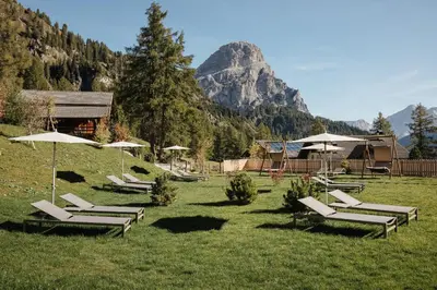 a group of lounge chairs and umbrellas with a mountain at Kolfuschgerhof Mountain Resort in Colfosco