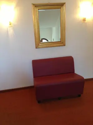 a mirror and a red chair in a room at Hotel Daniela in Merano