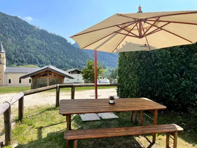 a wooden bench with an umbrella and a table at Conte Moro, ospitalità in Vanoi in Canale San Bovo