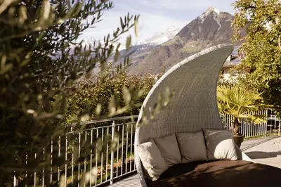a couch sitting on a balcony with mountains in the background at Residence Walchhof in Schenna