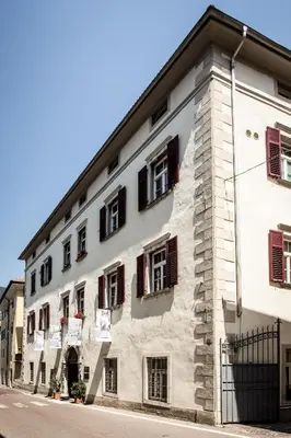 a large white building with red shuttered windows at Haus Noldin - historische Herberge - dimora storica in Salorno sulla Strada del Vino