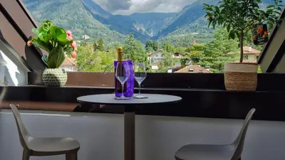 a table with a wine glass and two chairs at Appartamento Lichtenegg a Merano in Merano