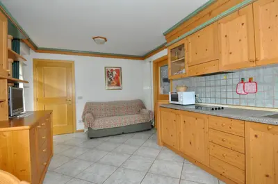 a kitchen with wooden cabinets and a bed in the background at Villetta Enrosadira in Vigo di Fassa