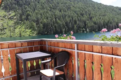 a table and a chair on a balcony with a lake at Schneiderhof in Valdurna