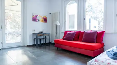 a red couch in a living room with two windows at Villa Anita Rooms in Bolzano