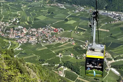 a gondola flying over a village in the mountains at Appartments Stoanegg in Parcines