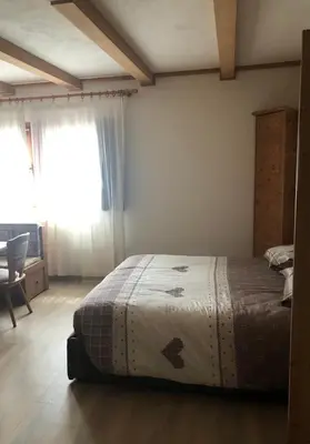 a bedroom with a bed and a chair and a window at Paradise Dolomiti flat in Falcade