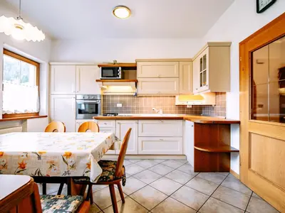 a kitchen with white cabinets and a table with chairs at Apartment Ardoney-1 by Interhome in Campitello