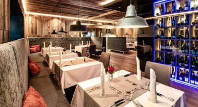 a restaurant with white tables and bottles of wine at Almhof Hotel Call in San Vigilio Di Marebbe