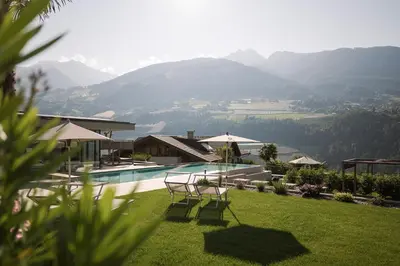 a large blue swimming pool with mountains in the background at Hotel Zirmerhof & Residence in Rifiano