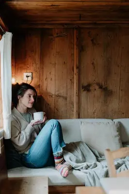 a woman sitting on a couch holding a cup of coffee at Mountain house Ebner in Selva dei Molini