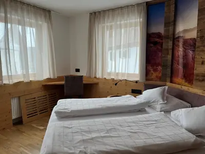 a bedroom with two beds and a desk and windows at A Sosta in Selva di Val Gardena