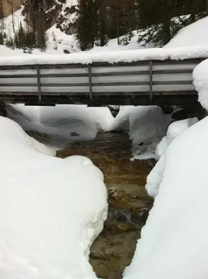 a bridge covered in snow with a stream under it at Piz Alpin B&B in Colfosco