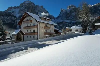 a building in the snow with mountains in the background at Piz Alpin B&B in Colfosco