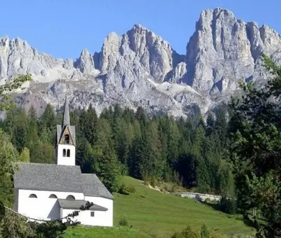 a church in a field with mountains in the background at Casa Felice in Caviola