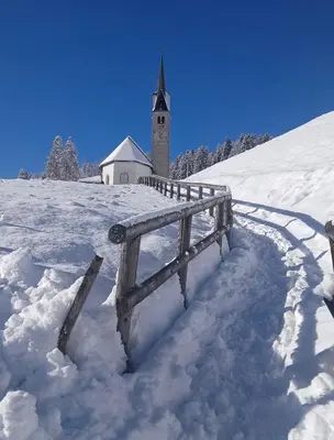 a church in the snow next to a fence at Casa Felice in Caviola
