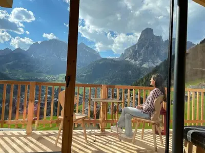 a woman sitting on a porch with a view of mountains at Luxury Chalet Liosa - Ski in Ski out - Amazing view in Corvara in Badia