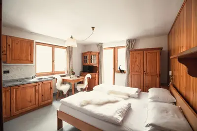 a bedroom with a bed and a kitchen with a table at PLOSE Parkhotel & Residence in Bressanone