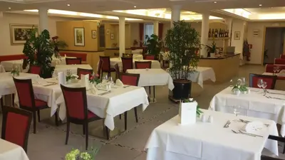 a restaurant with white tables and red chairs at Hotel Maximilian in Merano