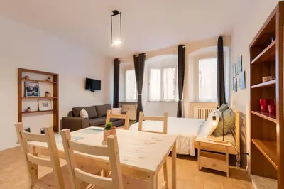 a kitchen and living room with a table and a room with a bed at Lauben Apartment Bolzano in Bolzano