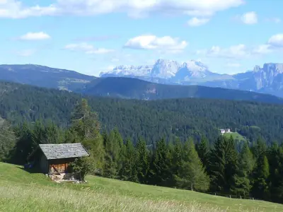an old cabin on a hill with mountains in the background at Rastlhof in Meltina