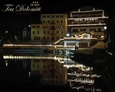 a night view of a building with lights in the water at Hotel TEA DOLOMITI - Lago di Alleghe - Monte Civetta in Alleghe