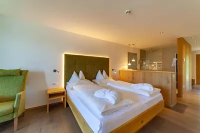 a bedroom with two beds and a green chair at Hotel Tyrol in Schenna