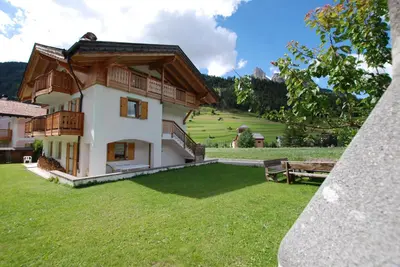 a view of a house with a green yard at Ciasa Rasom in Pozza di Fassa