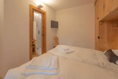 a bedroom with two beds with white sheets and a mirror at Casa Betulla in Cortina dʼAmpezzo