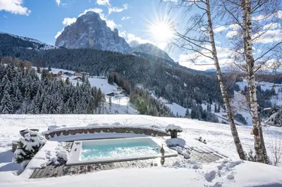 a hot tub in the snow with a mountain in the background at Chalet Villa Carolina in Selva di Val Gardena
