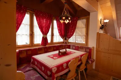 a room with a table and a couch and windows at Mansarda Le Genziane di Fiemme in Cavalese