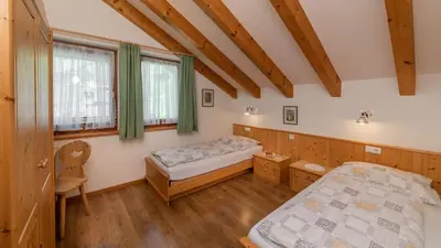 a bedroom with two beds and a chair at Haus Alpenjuval in Fundres