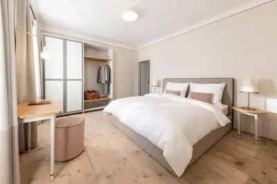 a white bedroom with a large bed and a desk at Smart Suites Kaltern - Apartments am Kalterer See in Caldaro