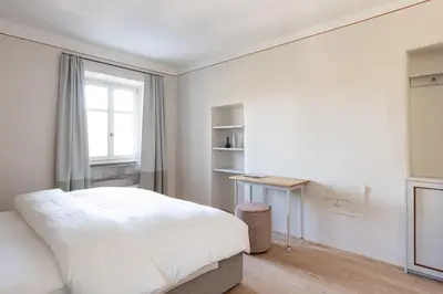 a white bedroom with a bed and a window at Smart Suites Kaltern - Apartments am Kalterer See in Caldaro