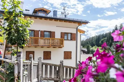 a house with a balcony and pink flowers at Appartamento Césa Ines in Arabba